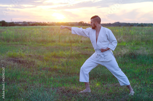 A man in a kimono trains karate in nature, a beautiful sunset and a copy of space. Martial arts, outdoor training.