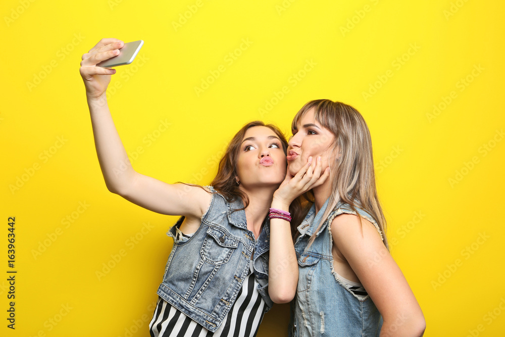 Two young woman making selfie on yellow background Two young woman making selfie on yellow background