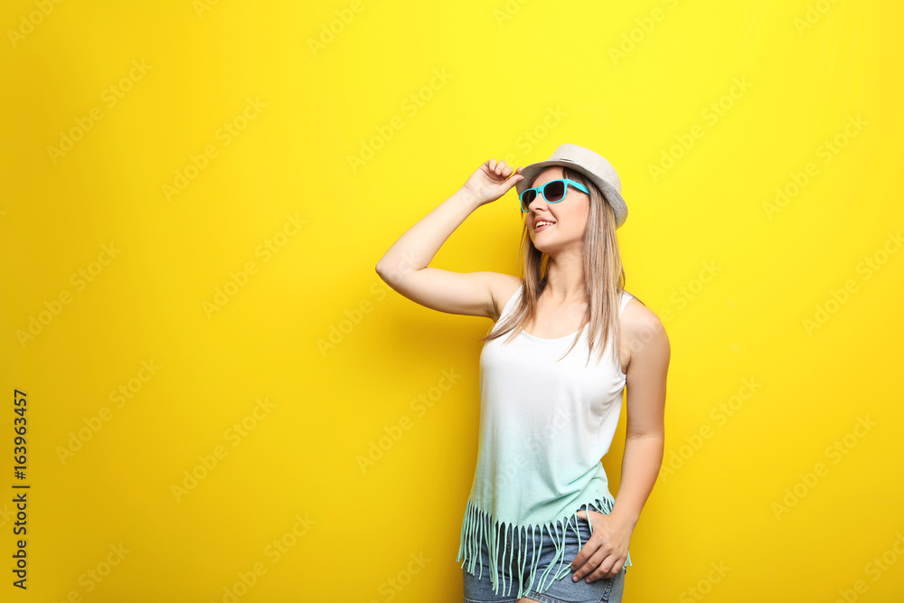 Portrait of young woman with sunglasses and hat on yellow background