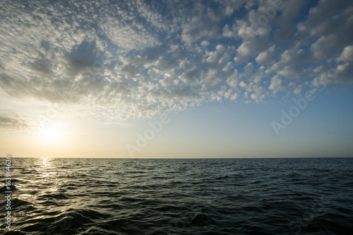 horizontal view of theAtlantic ocean in open waters at dawn with a partly cloudy sky and sunrise