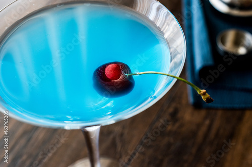Blue Moon Cocktail with cherry on wooden surface.