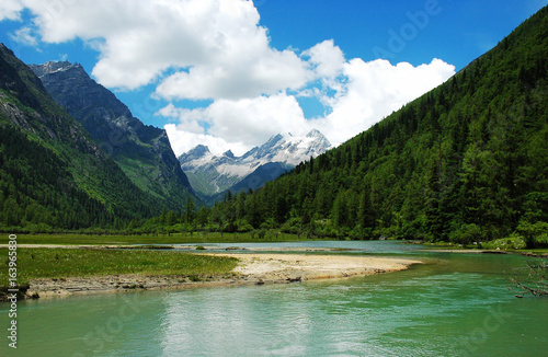 mountain valley and clear lake surface reflecting snow mountain and sky
