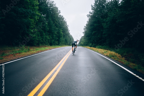 Selective focus shot of professional road cyclist riding down wet and windy mountain road in forest, on aero road bike from carbon