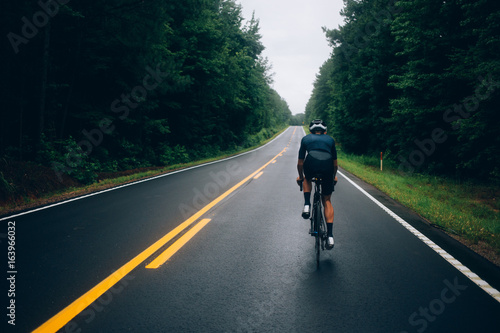 Fototapeta Naklejka Na Ścianę i Meble - Selective focus shot of professional road cyclist riding down wet and windy mountain road in forest, on aero road bike from carbon