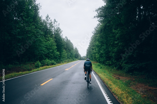 Fototapeta Naklejka Na Ścianę i Meble -  Selective focus shot of professional road cyclist riding down wet and windy mountain road in forest, on aero road bike from carbon
