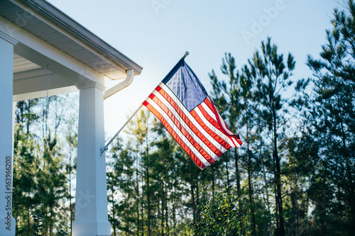 Front side of typical american porch colonial house with white traditional columns and pillars, beautiful garden in the back and forest