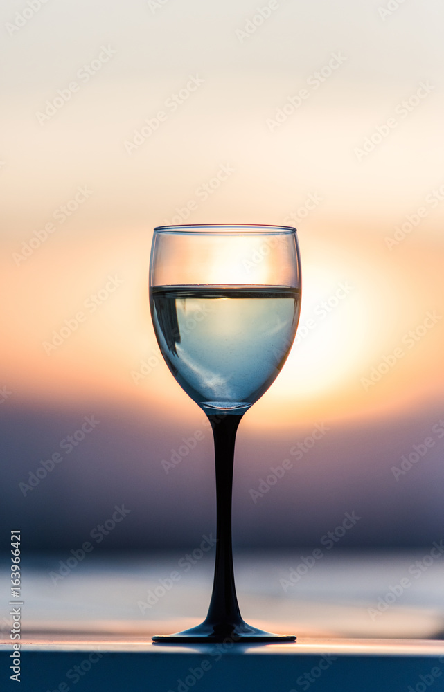 A glass with a white wine in the light of the setting sun. Vibrant alcohol background.