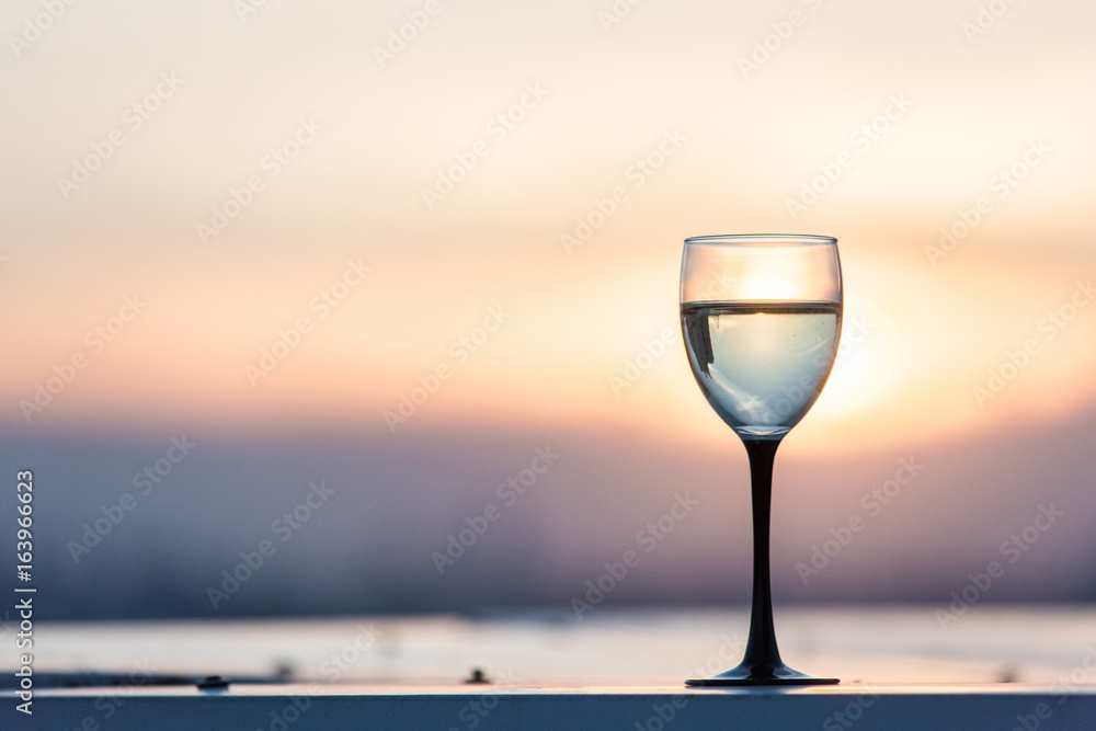 A glass with a white wine in the light of the setting sun. Vibrant alcohol background. A glass with a white wine in the light of the setting sun. Vibrant alcohol background.