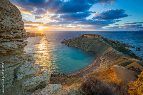 Mgarr, Malta - Panorama of Gnejna bay, the most beautiful beach in Malta at sunset with beautiful colorful sky and golden rocks taken from Ta Lippija photo