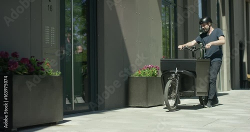 Handsome man takes out a case of his cargo bike and rings a door bell photo