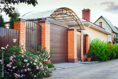 A brown fence made of polyprofile with a canopy in a modern style with brick columns, the design of a country house. photo