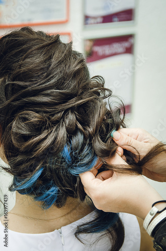 Closeup of a professional hairdresser's hands doing a hairstyle in a beauty salon. Brunette, in the hair some of the strands are painted blue. The concept of fashionable stylish hairstyle.