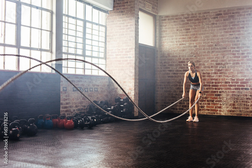 Athlete exercising in gymnasium using training ropes.