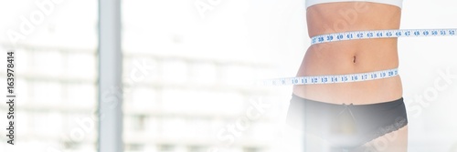 Slim healthy woman holding measuring tape by window