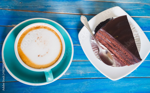 Top view of hot latte or capucino coffee in  blue club on blue vintage wooden table background with Chocolate cake