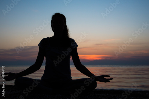 Silhouette of yogi girl in lotus pose with sunset in background
