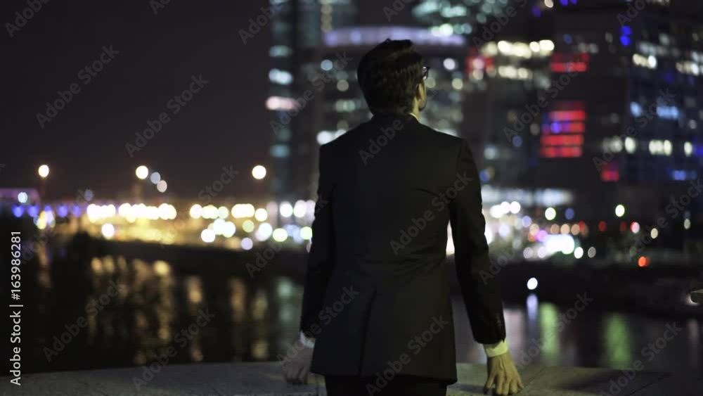 Young and handsome businessman in a suit putting on his glasses, looking at skyscrapers and turning to the viewer. Handheld real time medium shot Young and handsome businessman in a suit putting on his glasses, looking at skyscrapers and turning to the viewer. Handheld real time medium shot
