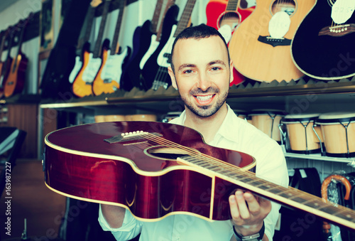 Guy choosing guitar in music shop.