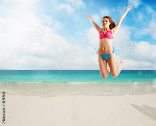 Woman in bikini swimsuit jumping from joy on tropical beach