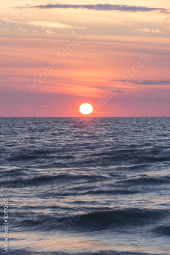 Glowing sun setting on horizon over low rolling waves in water