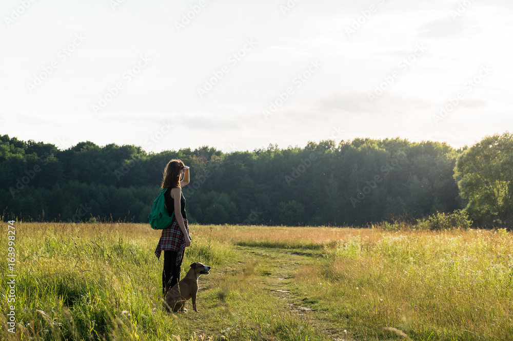 Adventure time for a young female and her staffordshire terrier. Young female person looks in distance and her pet dog sits next to her in the grass Adventure time for a young female and her staffordshire terrier. Young female person looks in distance and her pet dog sits next to her in the grass