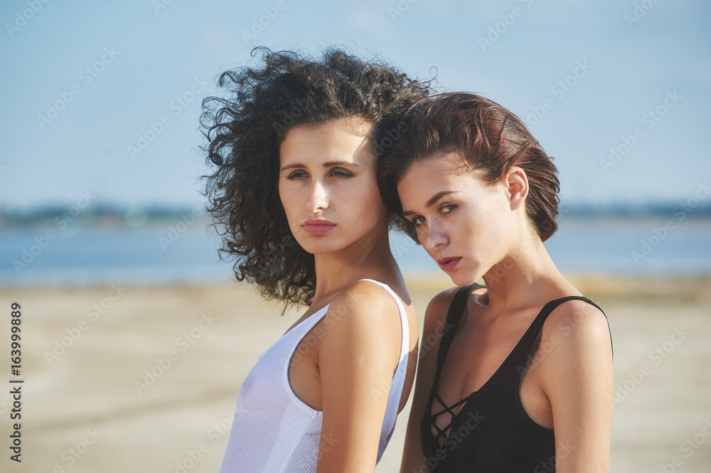 two girls model posing lying on the sand . The concept of summer clothes two girls model posing lying on the sand . The concept of summer clothes