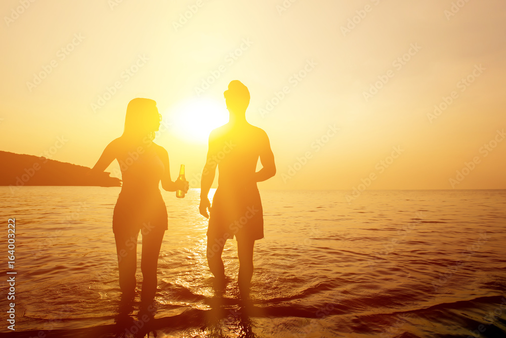 Silhouette of couple walking in seawater at the beach in twilight sunset