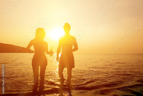 Foto Silhouette of couple walking in seawater at the beach in twilight sunset