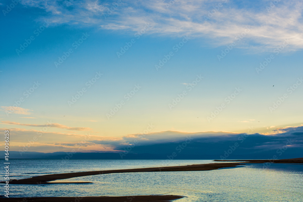 Obraz premium rippled surface of cold lake under sky with fluffy clouds at sunrise 