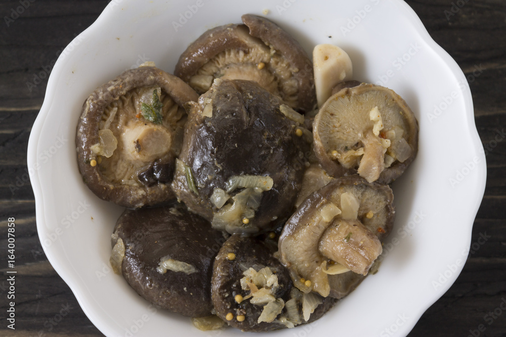 Marinated mushrooms in a white bowl on a wooden table Marinated mushrooms in a white bowl on a wooden table