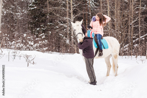 Girl, horse trainer and white horse in a winter