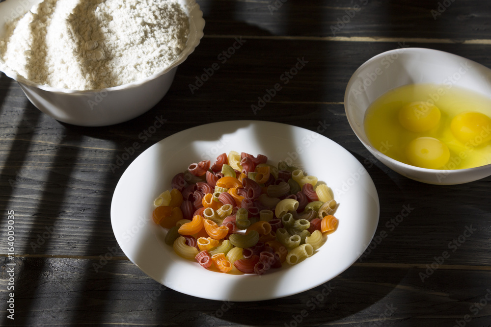 Raw colored pasta in a white plate on a wooden table