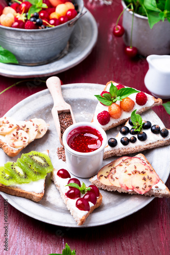 Fruit toast on red background. Healthy breakfast. Clean eating. Dieting concept. Grain bread slices with cream cheese and various fruit, berries, seeds. Vegetarian.