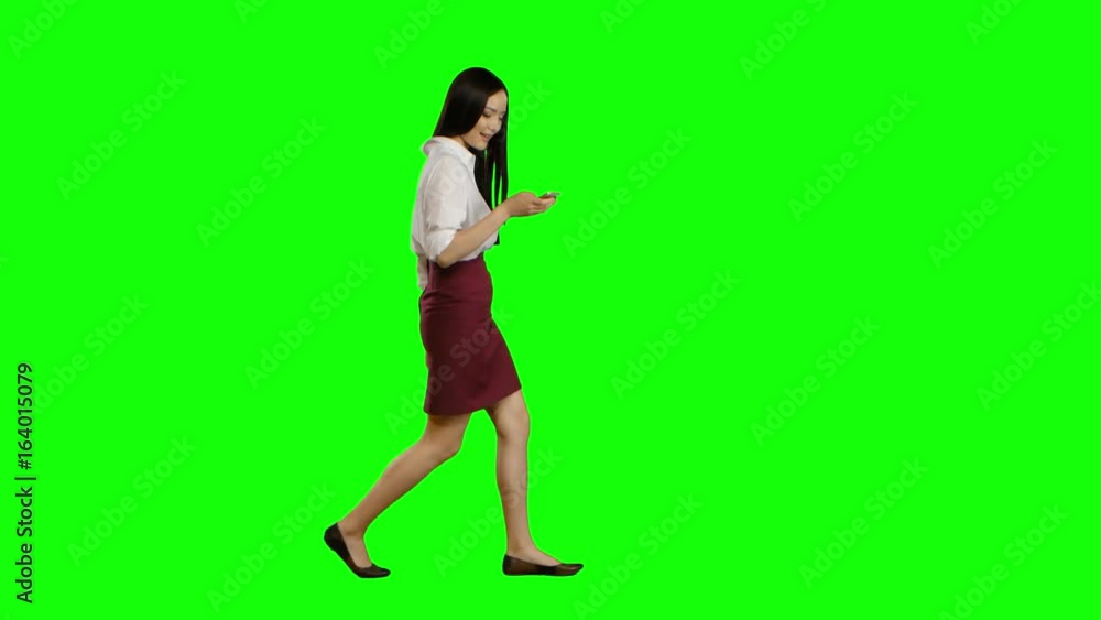 Girl walks and holds a phone and looks at photos. Green screen. Side view Girl walks and holds a phone and looks at photos. Green screen. Side view