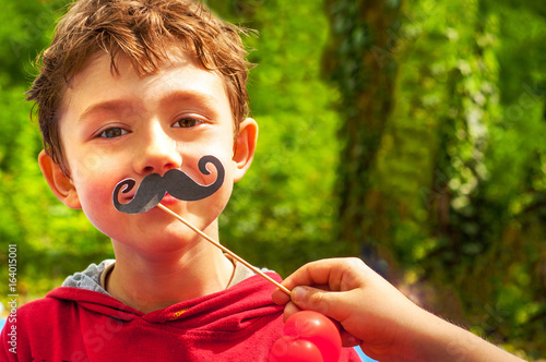 A boy trying on a paper mustache on stick photo