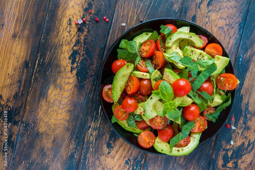 Φωτογραφία Vegetarian salad with avocado, cherry tomatoes and basil leaves on a black plate on the wooden rustic table, top view