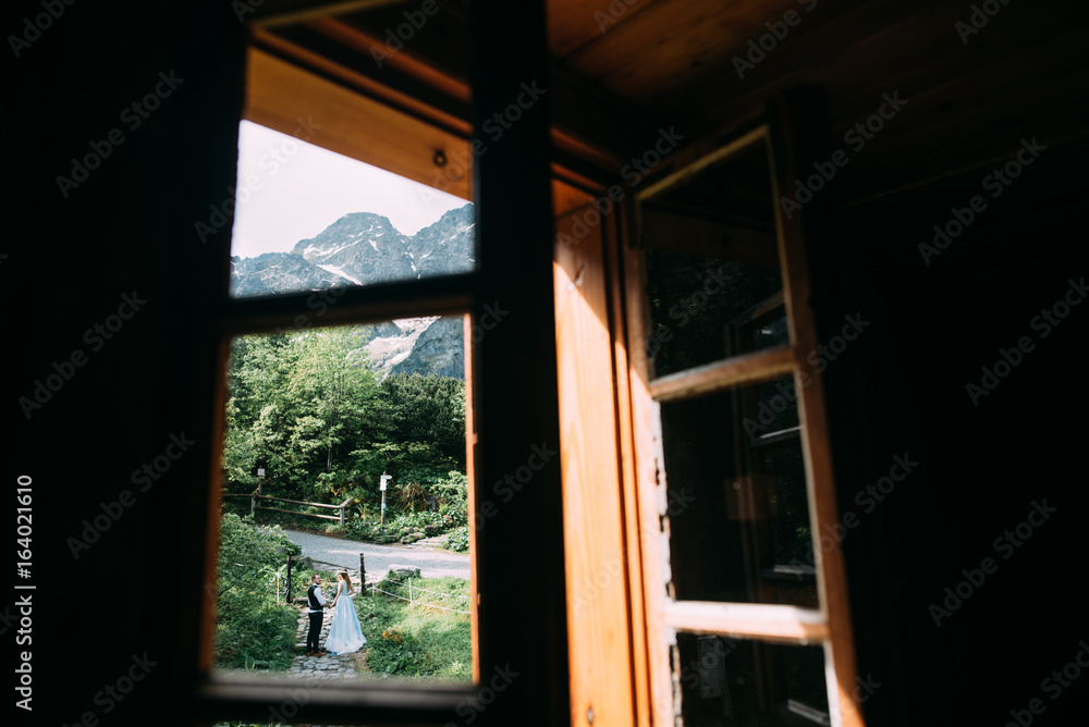 Fototapeta premium a view through a window facing the bride and groom with mountain views