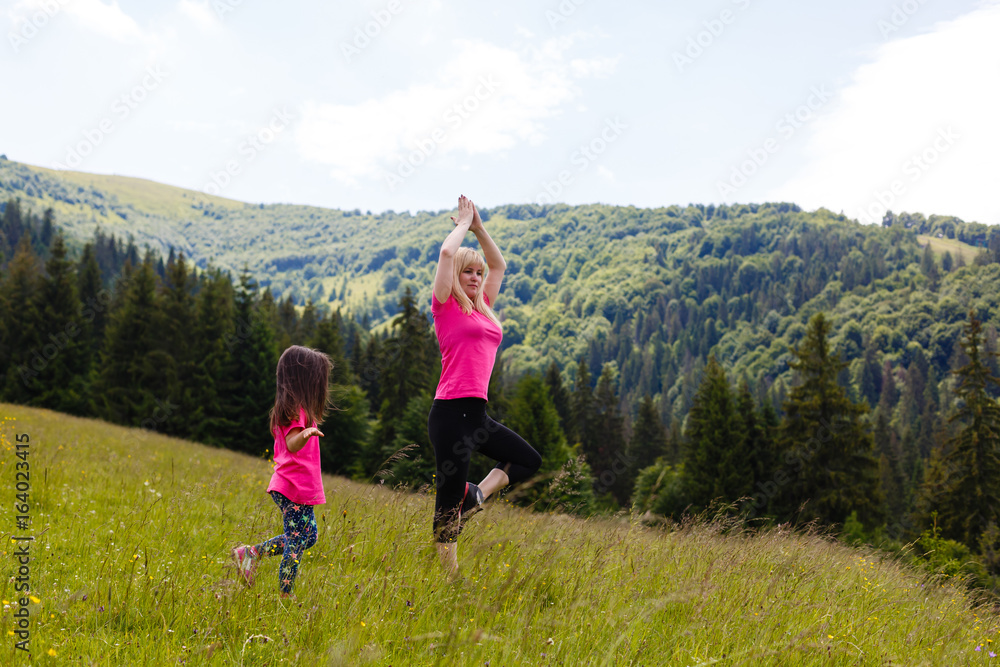 Mother and daughter doing yoga Tree pose at top of mountain Mother and daughter doing yoga Tree pose at top of mountain