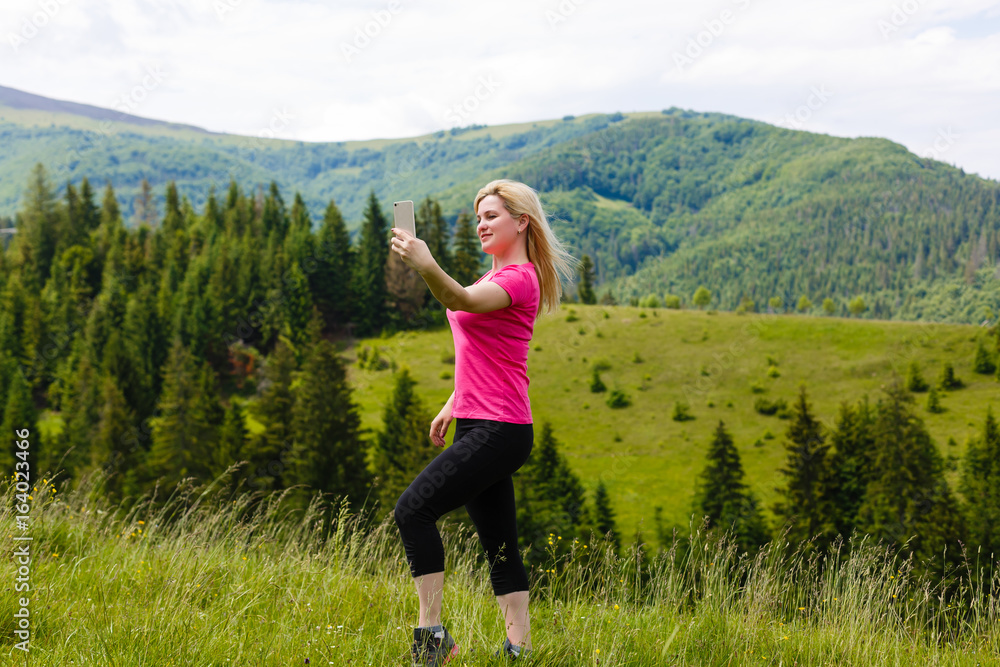 With technology, traveling is easier. Beautiful young modern girl traveler with travel bag smiling and taking pictures or doing selfie on a background of mountains or nature With technology, traveling is easier. Beautiful young modern girl traveler with travel bag smiling and taking pictures or doing selfie on a background of mountains or nature