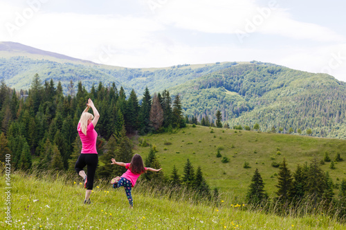 Mother and daughter doing yoga Tree pose at top of mountain