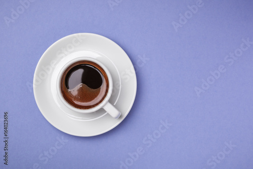 Cup of espresso with saucer on blue background.