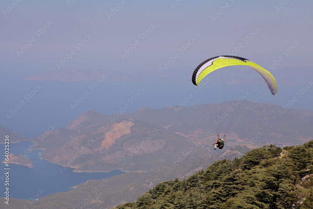 Paraglider flies in the sky. Panoramic bird's-eye view on Turkey, Oludeniz, Mediterranean. Paragliding is a free flying sport where the pilot launches themselves by foot. Paraglider flies in the sky. Panoramic bird's-eye view on Turkey, Oludeniz, Mediterranean. Paragliding is a free flying sport where the pilot launches themselves by foot.