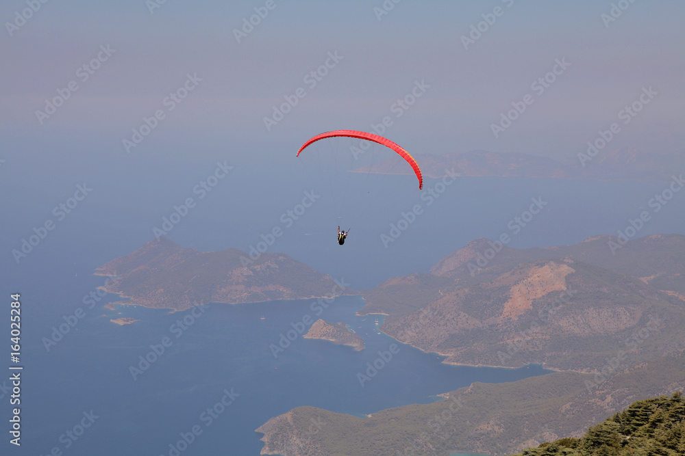 Paraglider flies in the sky. Panoramic bird's-eye view on Turkey, Oludeniz, Mediterranean. Paragliding is a free flying sport where the pilot launches themselves by foot. Paraglider flies in the sky. Panoramic bird's-eye view on Turkey, Oludeniz, Mediterranean. Paragliding is a free flying sport where the pilot launches themselves by foot.