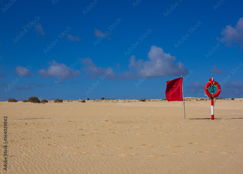 Swimming circle. Life buoy red color on beach with bright sand and sky background. Two warning signs. Safety guard, lifebuoy, lifeguard. Vacation at ocean. Swimming circle. Life buoy red color on beach with bright sand and sky background. Two warning signs. Safety guard, lifebuoy, lifeguard. Vacation at ocean.