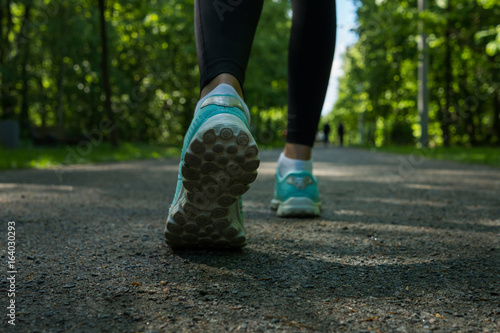 Close up shoe of runner feet running on road at public park.Woman fitness jog workout wellness concept.