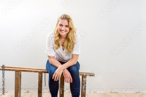 lachende junge Handwerkerin sitzt auf einer Leiter in ihrem neuen Haus und plant die Umbauarbeiten