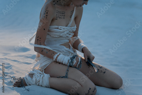 Vászonkép Girl in image of Egyptian mummy sits on sand with  metal chain and knife in her hands
