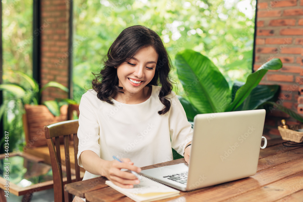 Young business woman sitting at table in cafe and writing in notebook. Laptop, smartphone and cup of coffee on table. Young business woman sitting at table in cafe and writing in notebook. Laptop, smartphone and cup of coffee on table.