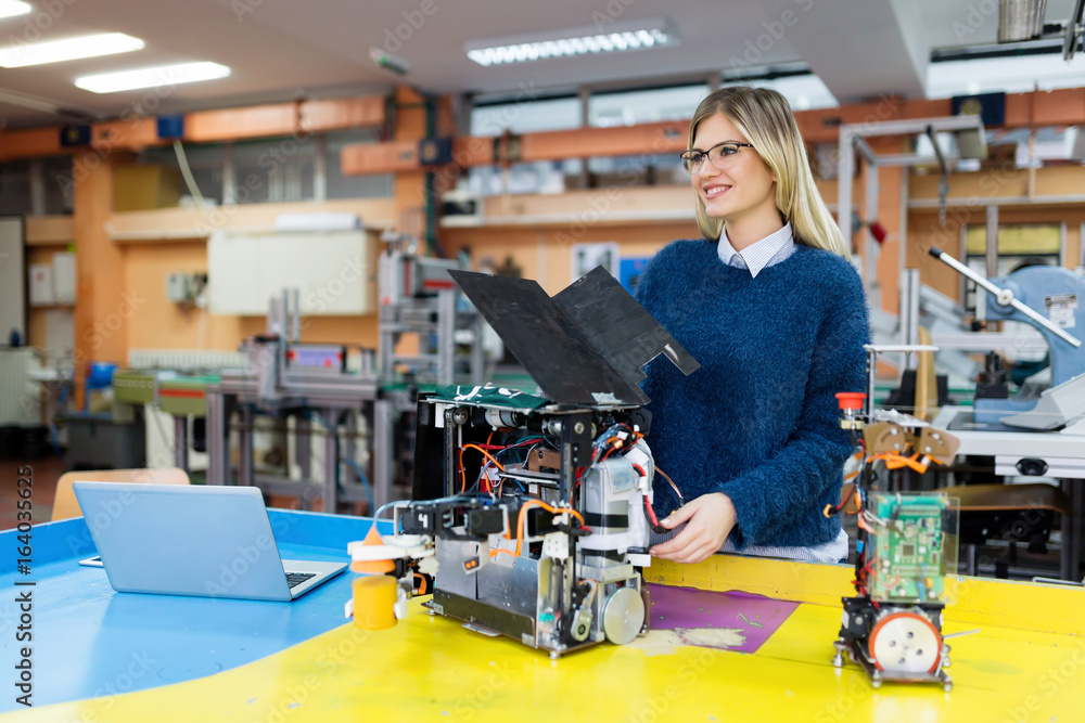 Young beautiful female engineer testing robot in workshop