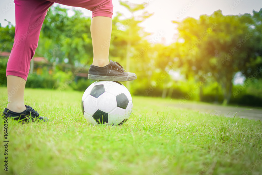 Boy with ball on green grass with sunset background.